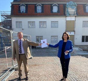 Staatssekretärin Daniela Schmitt übergibt Bürgermeister Christoph Burkhard auf dem Festplatz vor dem Museum den Förderbescheid zum barrierefreien Ausbau